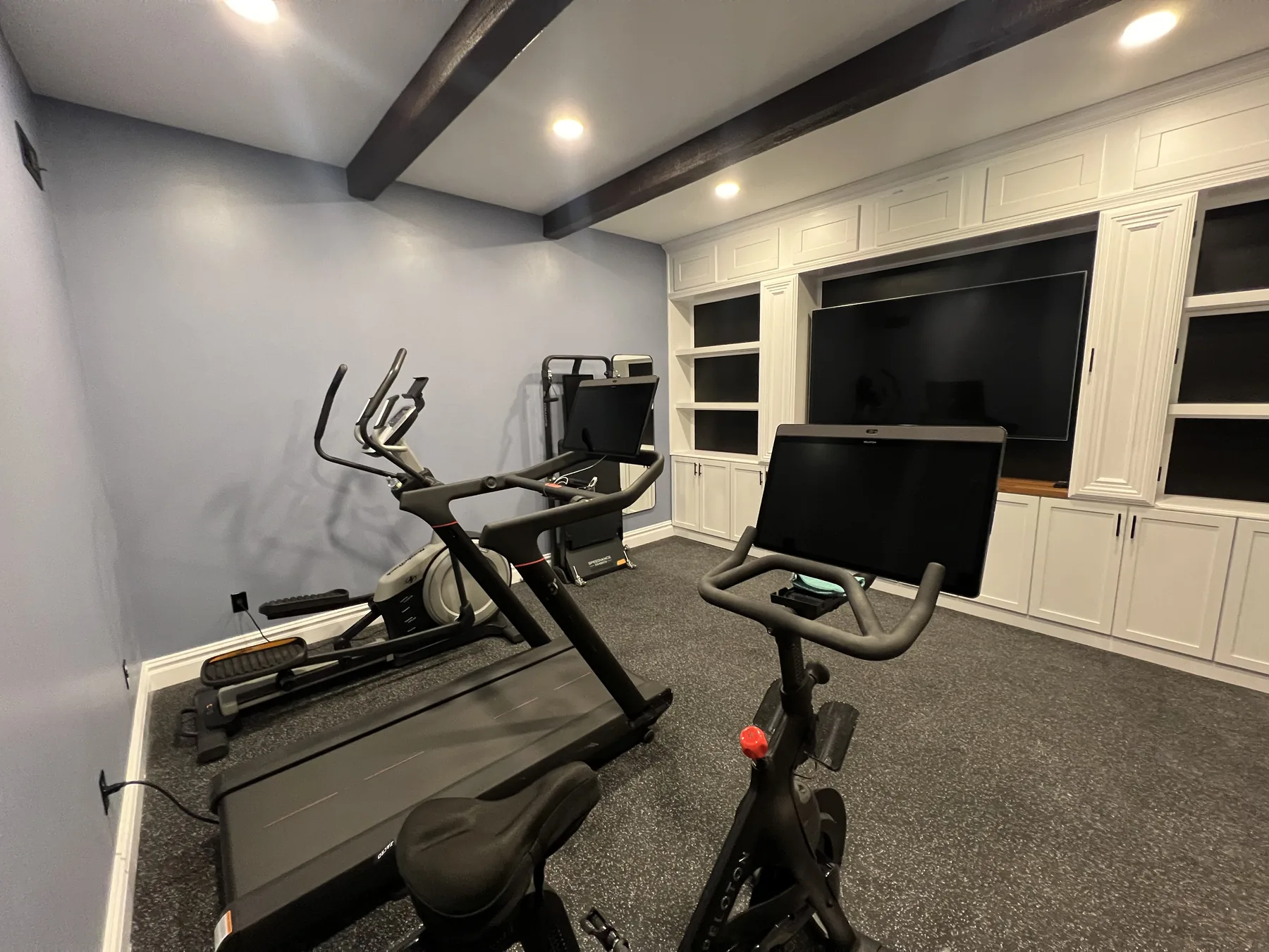 Finished basement set up as a home gym with cabinetry and a wall mounted television