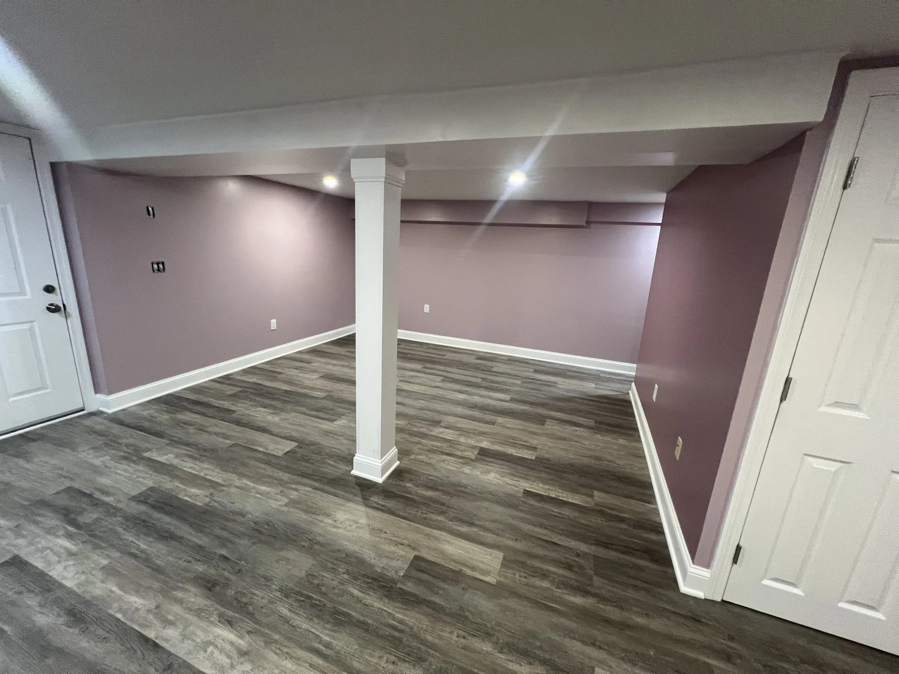 Finished basement with plank flooring, painted walls and a support post cased in
