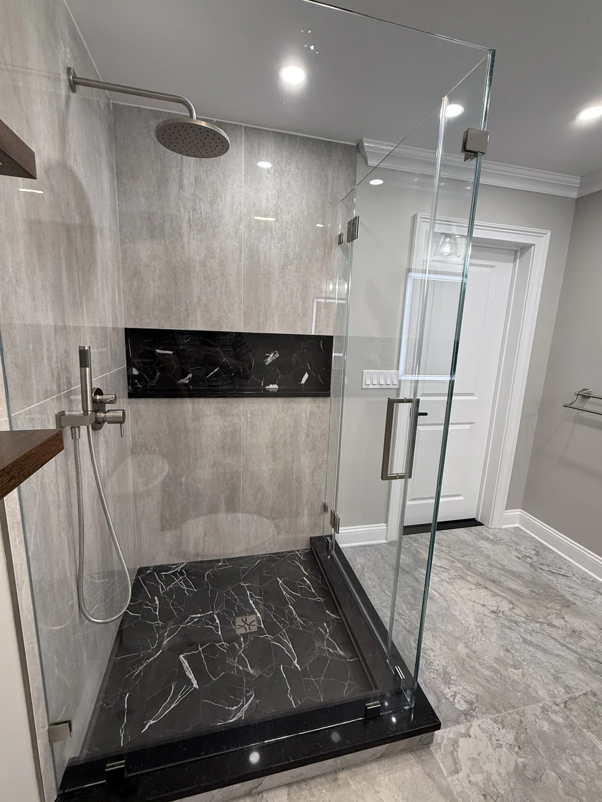 Glass shower with veined wall tile, a black marble base and a brushed shower head