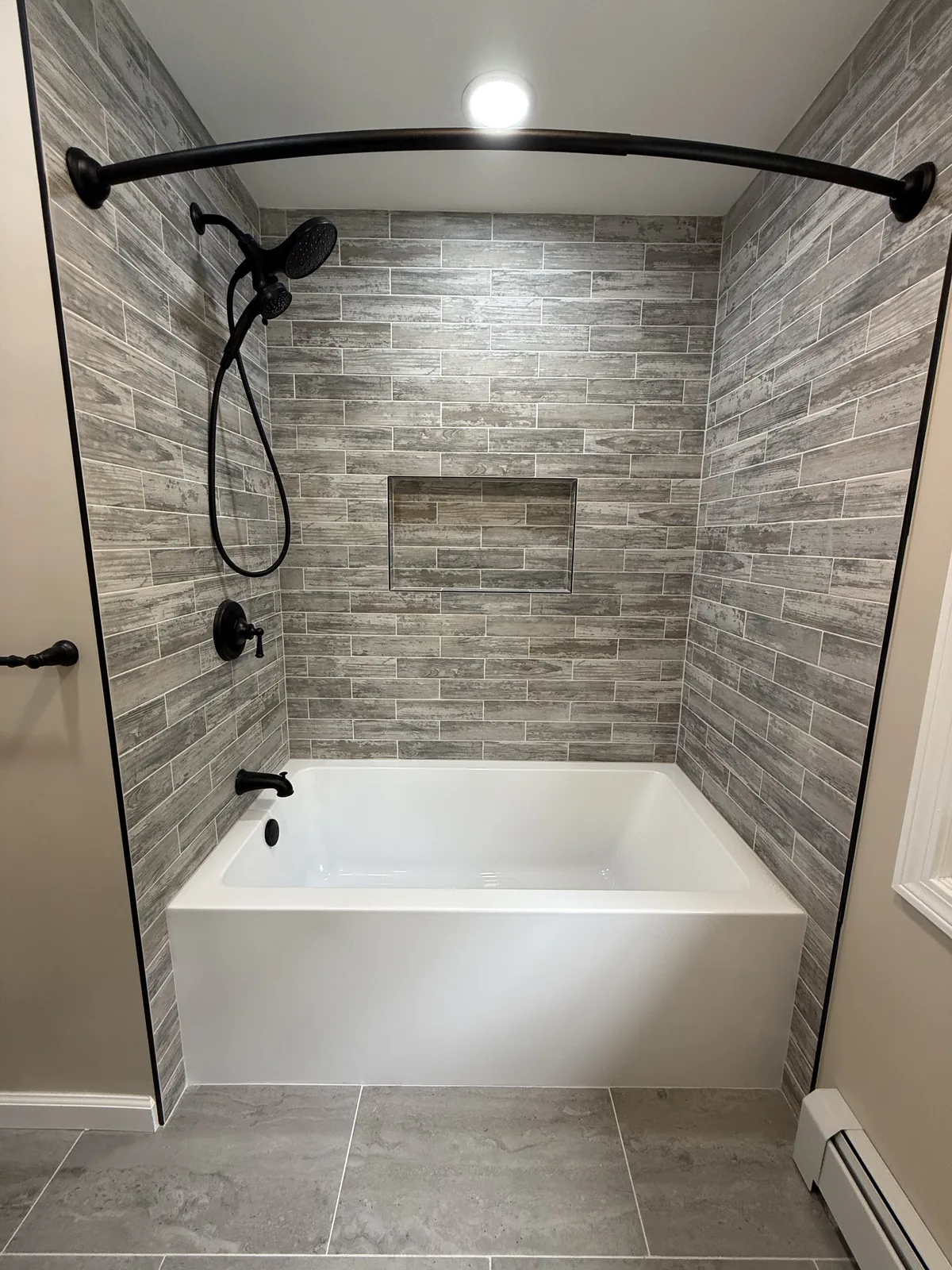 Bathroom with a gray tiled tub surround, a black curved rail and a niche