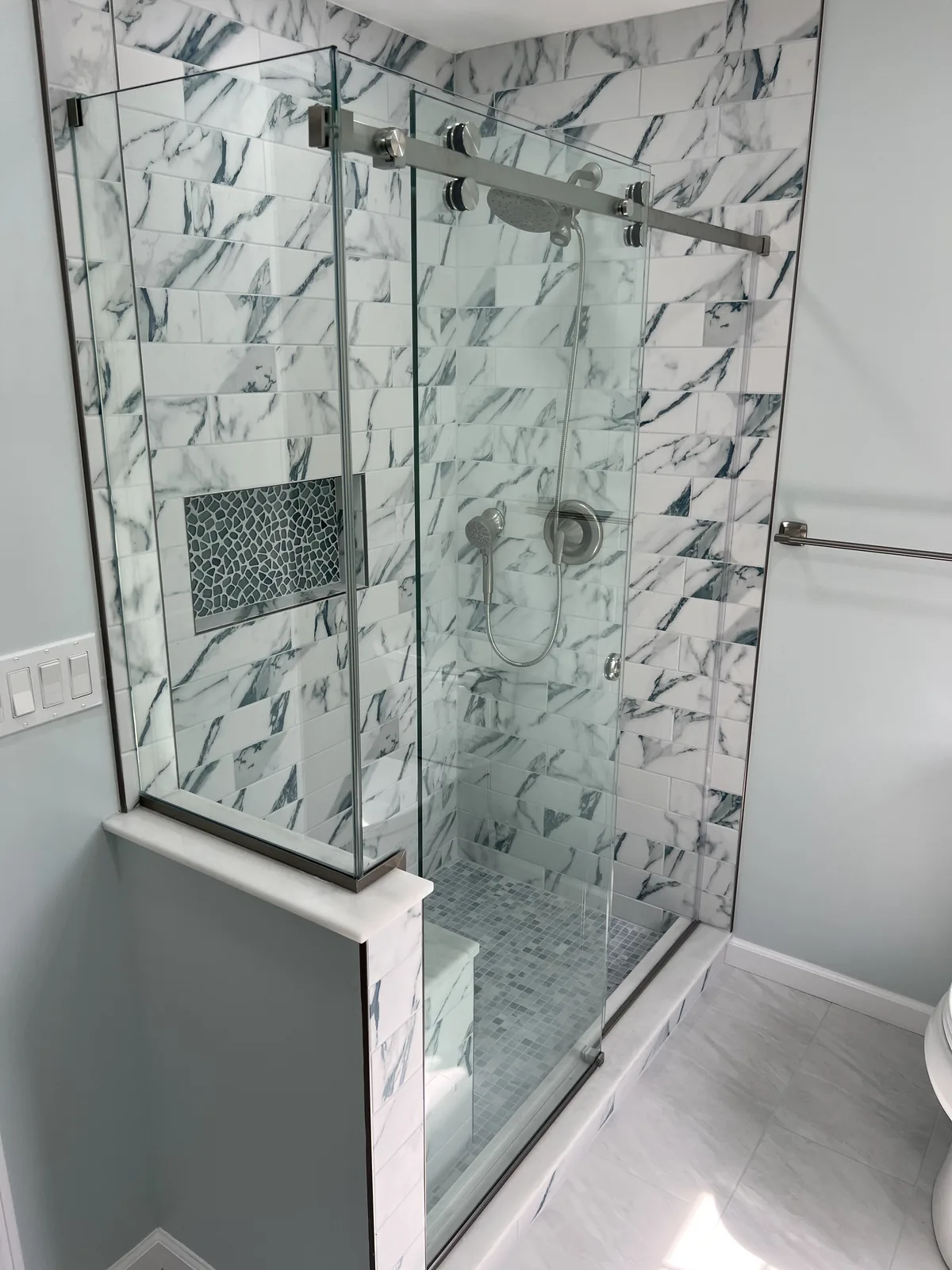 Marble tiled shower with a frameless glass return and a built in bench