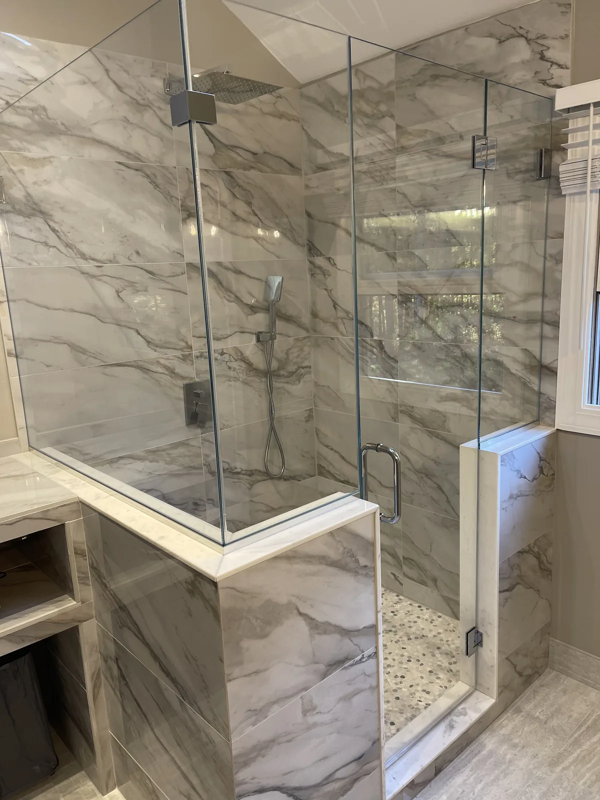 Walk in shower clad in marble with a frameless glass surround and a built in bench