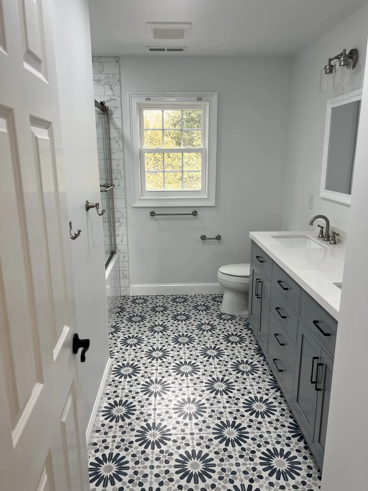 Guest bathroom with black and white patterned floor tile, a gray vanity and a white door