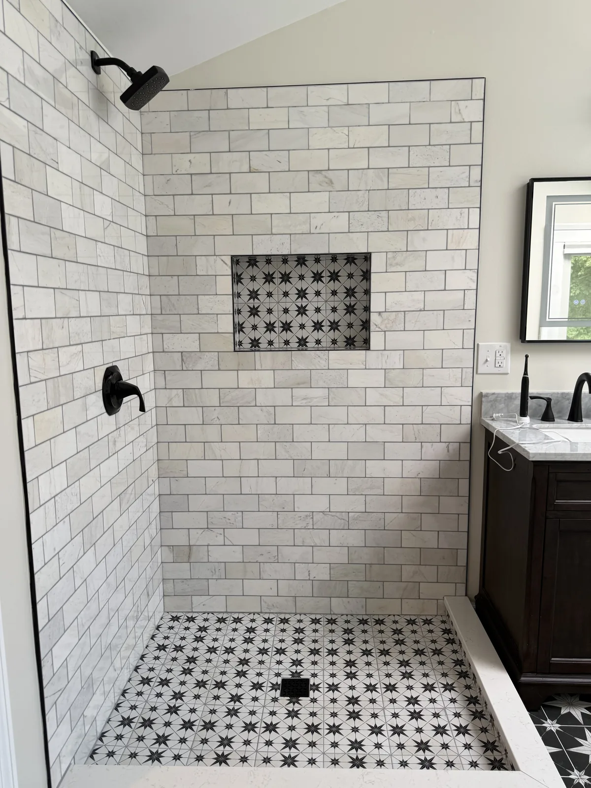 Shower lined in white subway tile with a mosaic floor and black fixtures