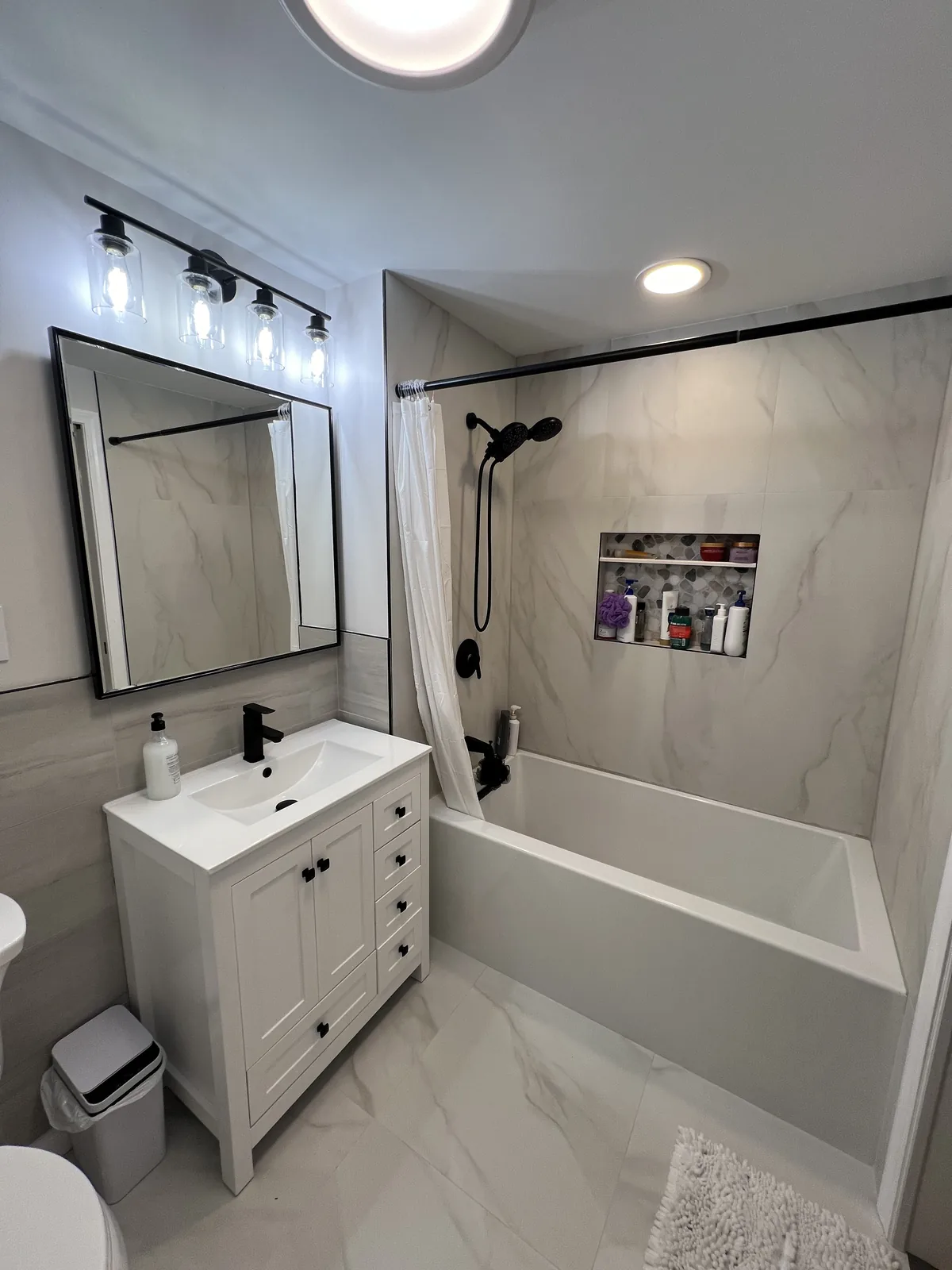 Bathroom with a white vanity, black fixtures and a tub under the window