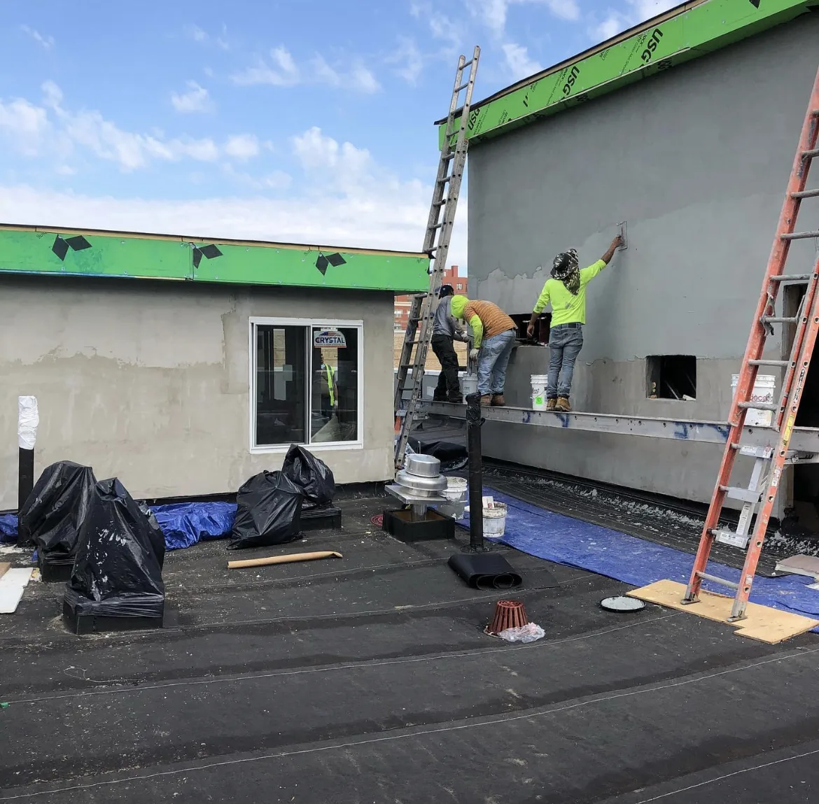 Two workers rolling coating onto the exterior wall of a commercial building