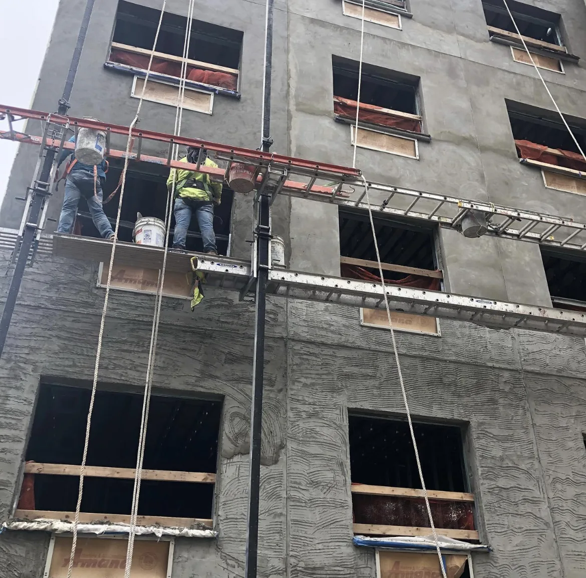 Crew working from a suspended stage on a concrete building facade