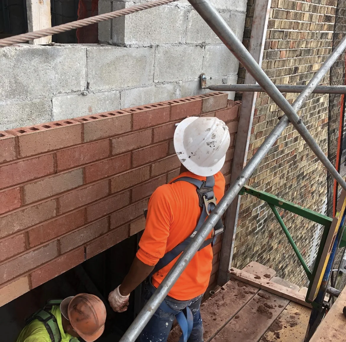 Mason in high visibility gear repairing brickwork behind scaffolding
