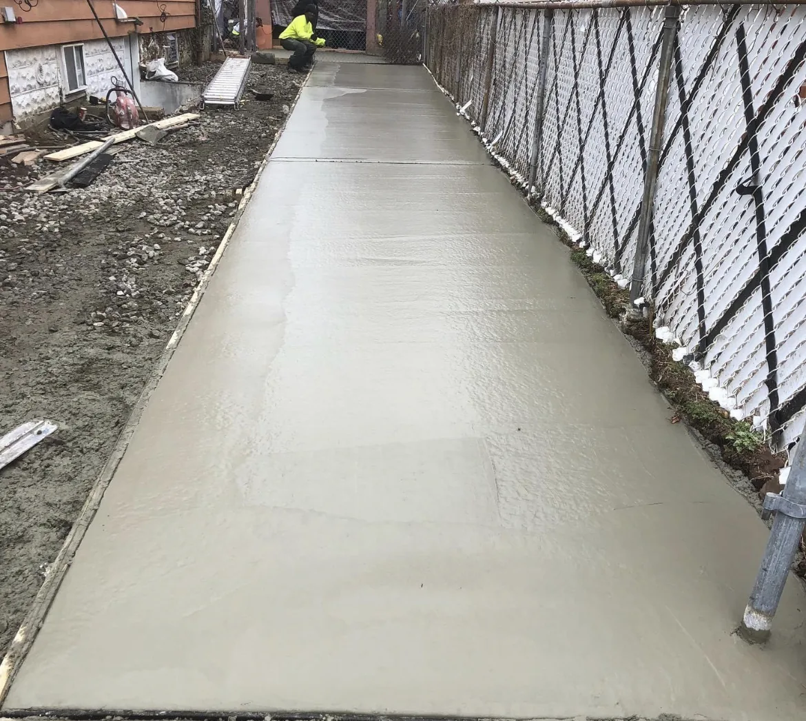 Freshly poured and floated concrete walkway between fencing