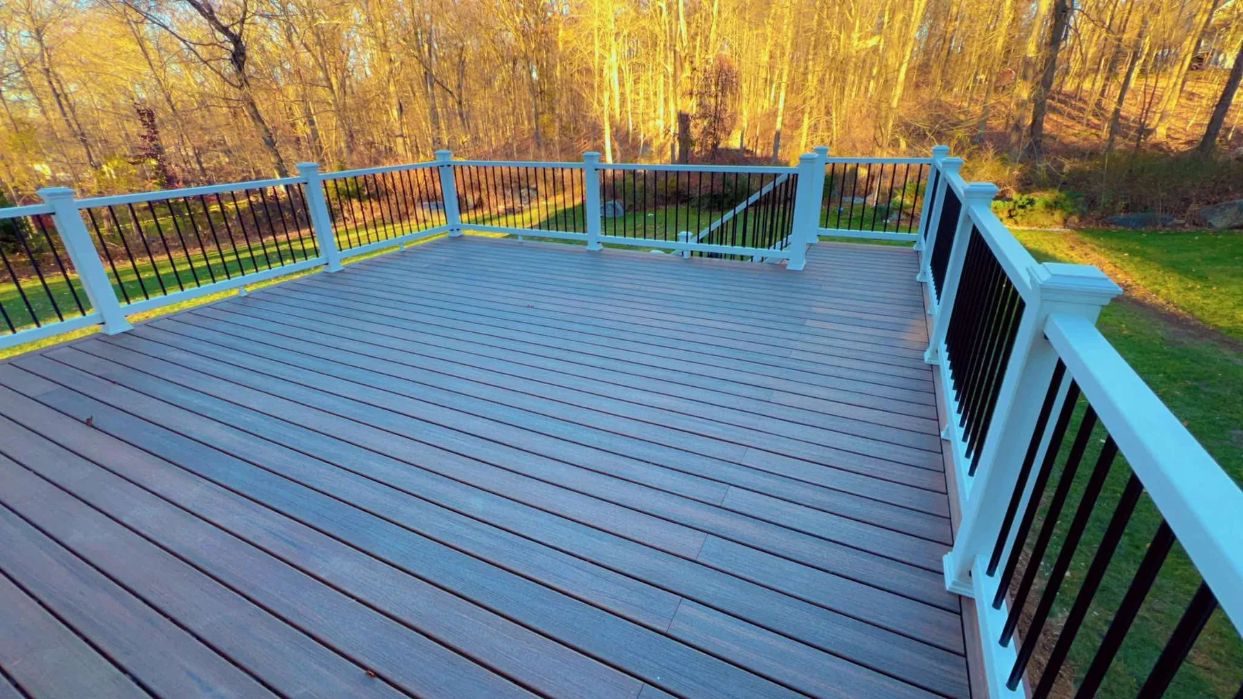 Composite deck with black aluminum railings backing onto autumn woods