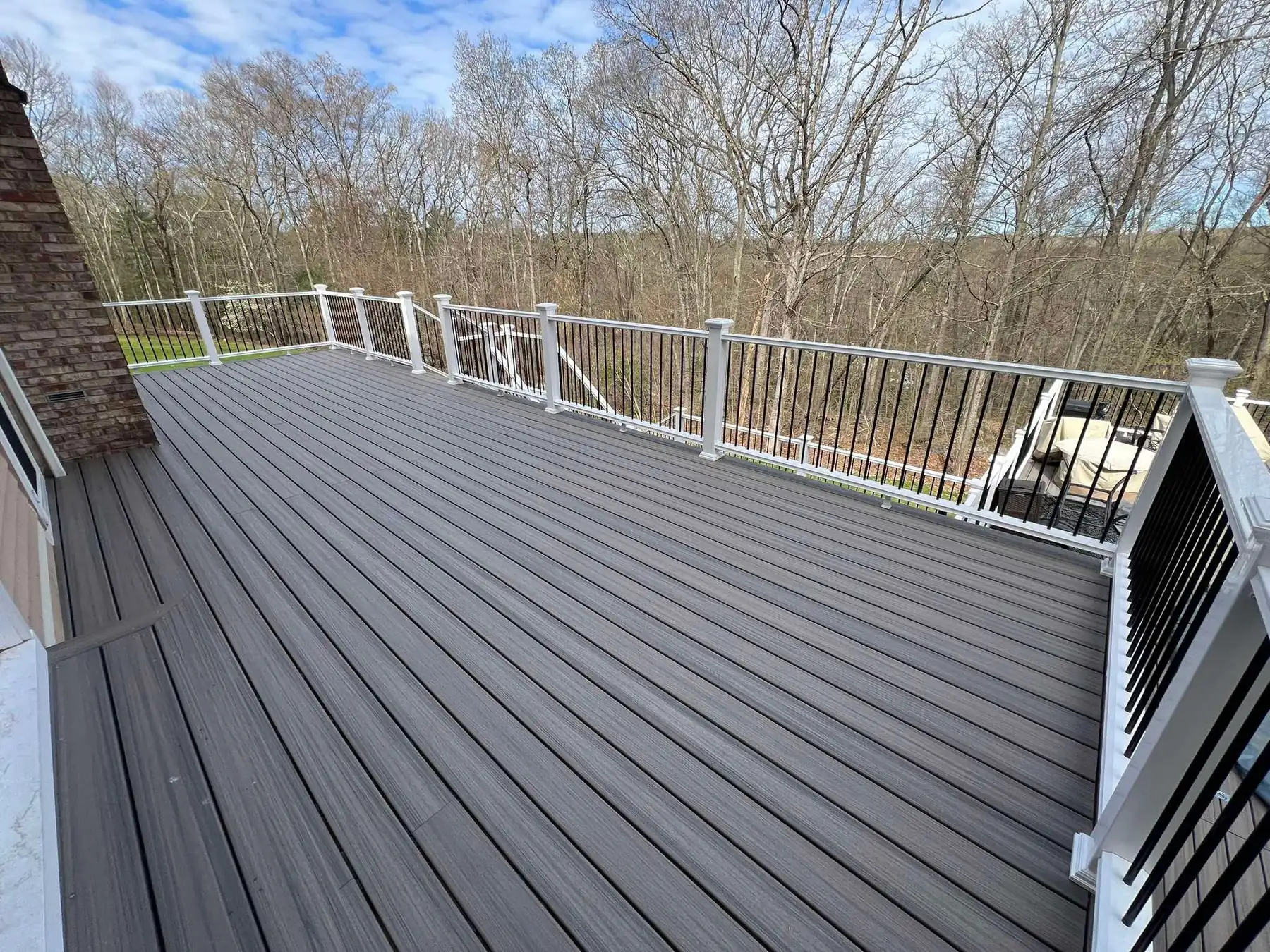 Gray composite deck with white railings running along the back of a house