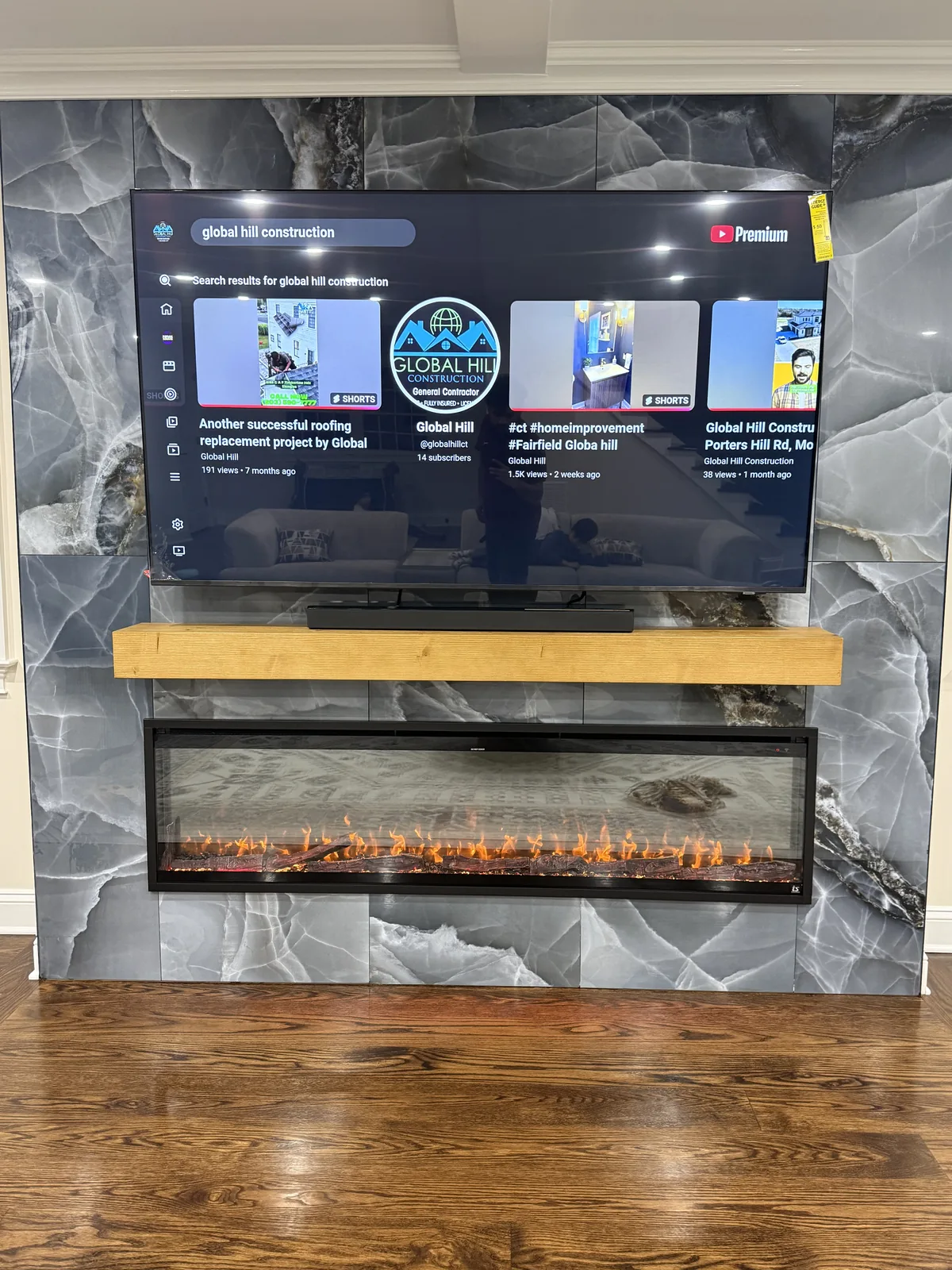 Marble fireplace wall with a timber mantel, a linear fireplace and a mounted television