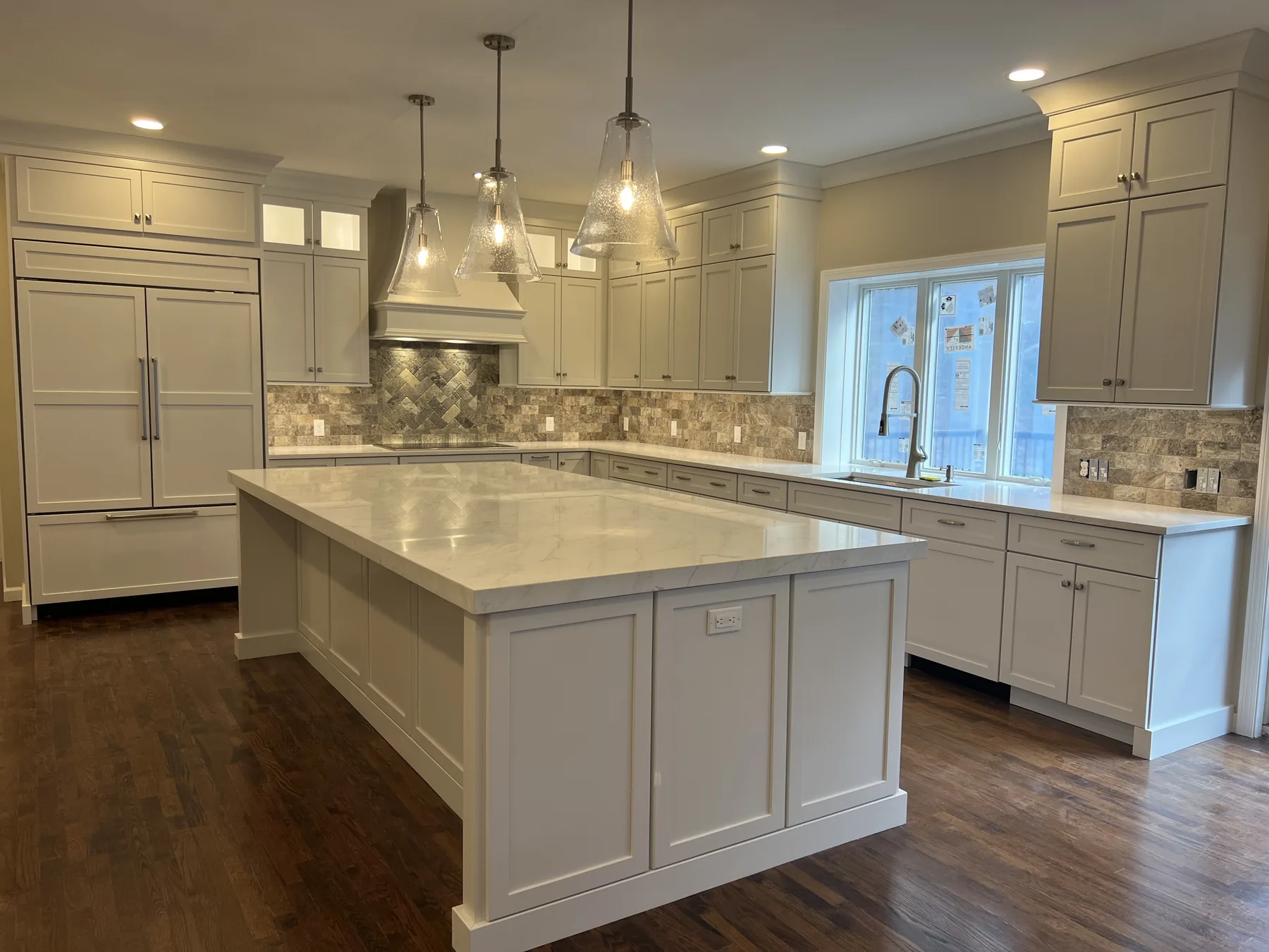 White kitchen with a long island, pendant lights and glass doors to the yard