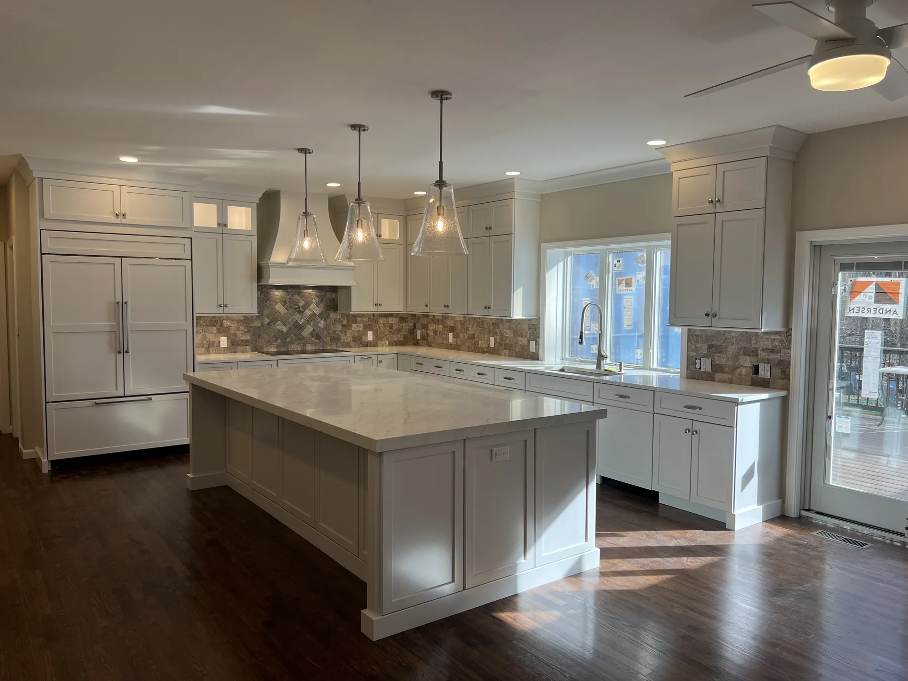 White shaker kitchen with a large island, stone backsplash and dark hardwood floors
