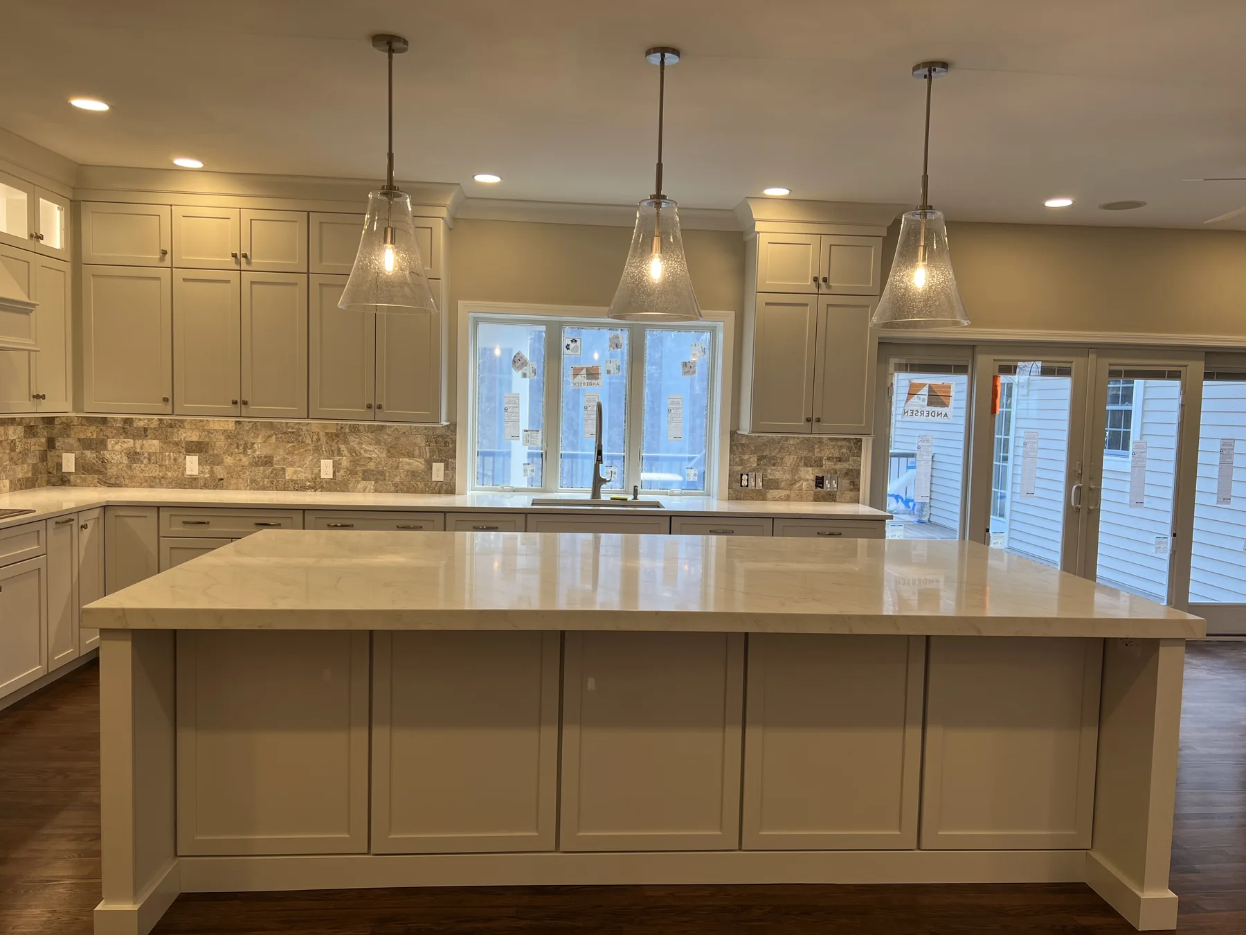 Open kitchen with a long white island, pendant lights and glass doors to the yard