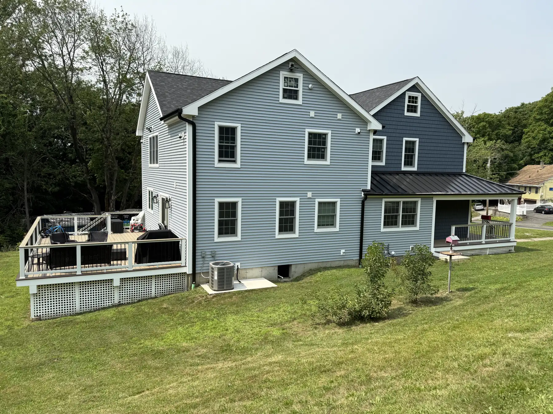 Side of a custom home with gray siding, a standing seam roof and a raised deck