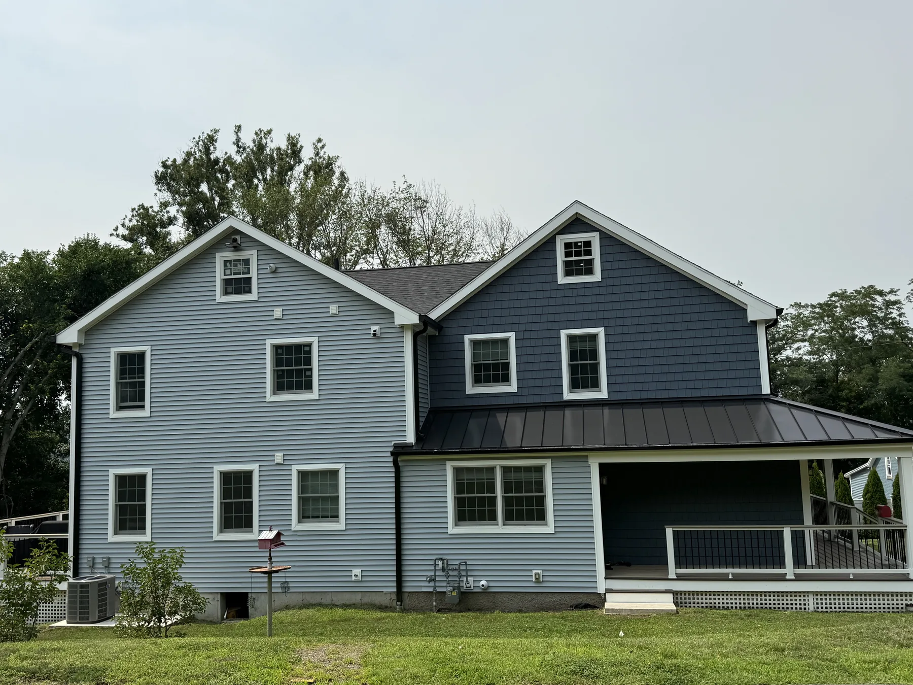 Rear of a newly built home with gray siding, black windows and a covered porch