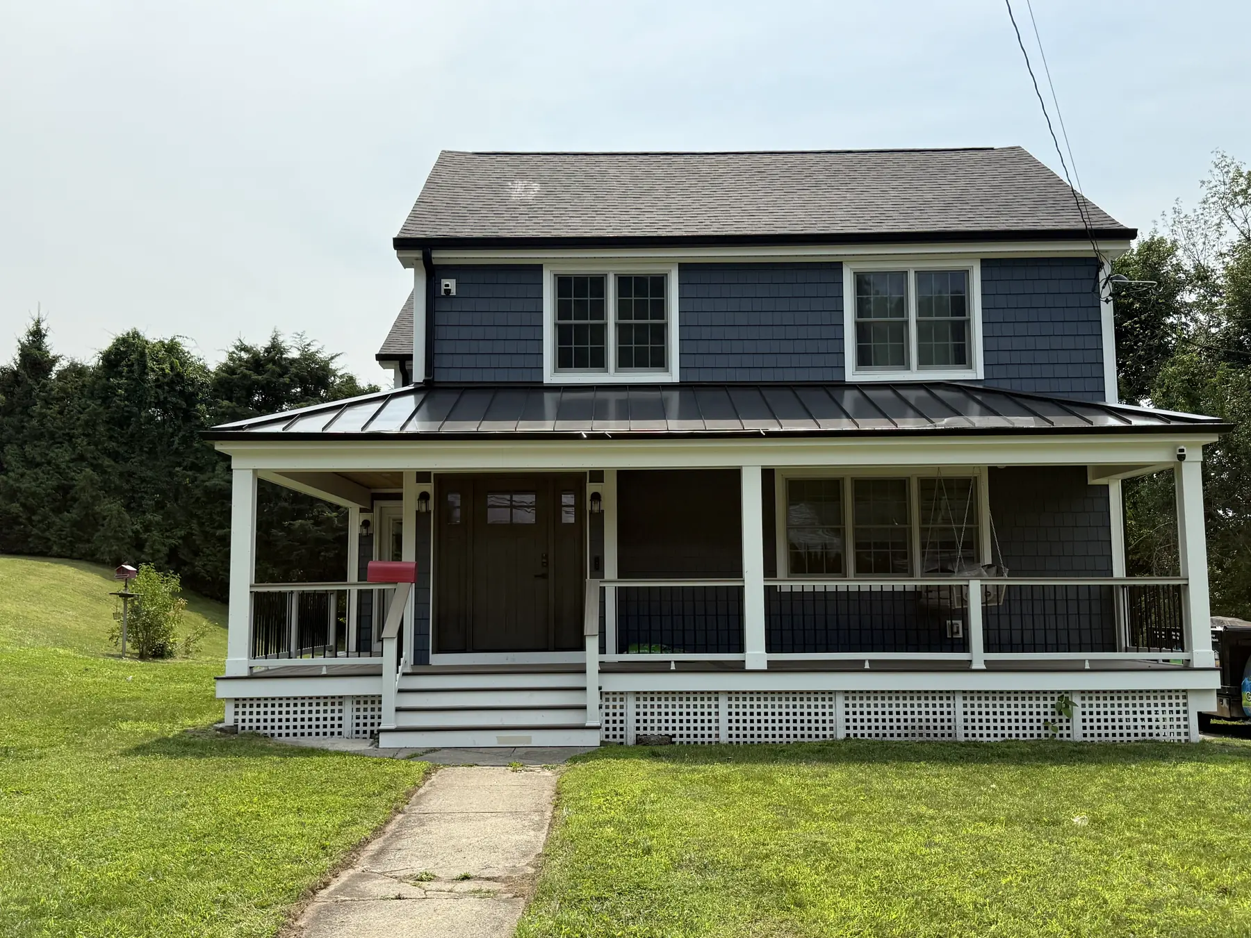 Newly built home with grey siding, a standing seam roof and a covered front porch