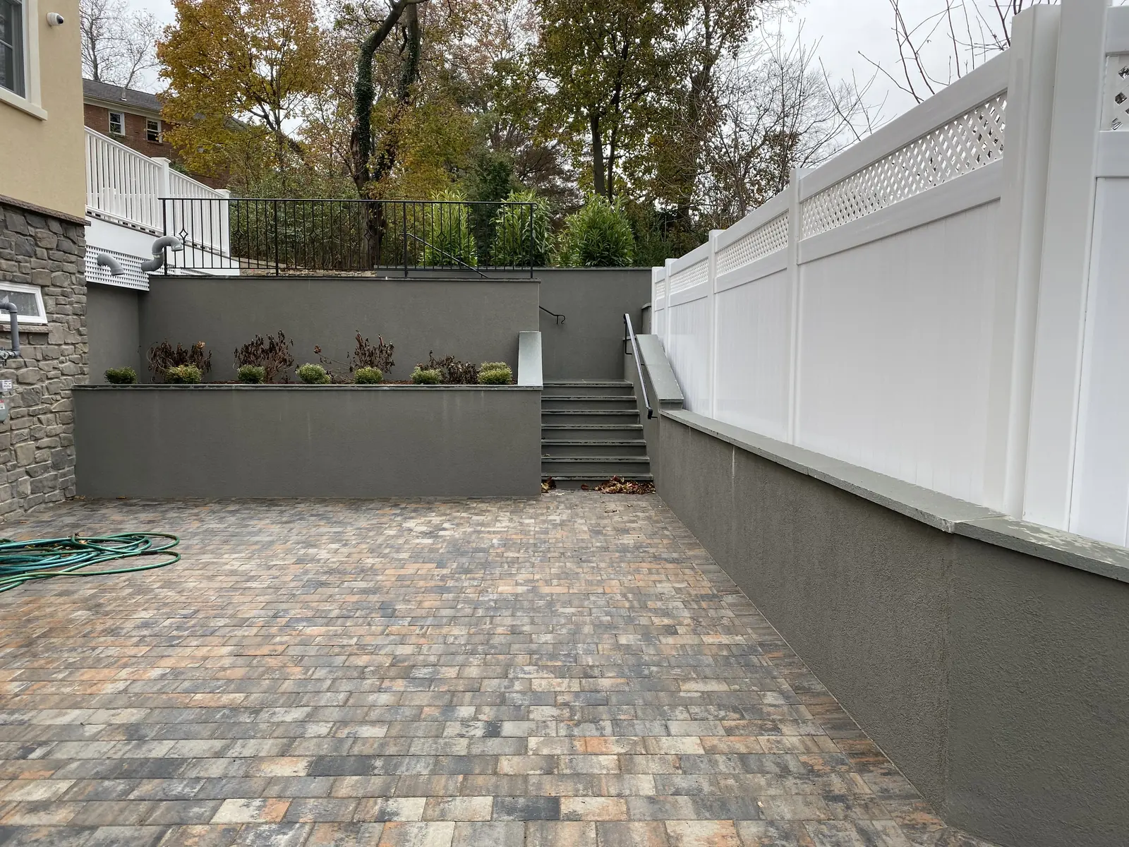 Paver driveway and retaining wall beside a white vinyl fence
