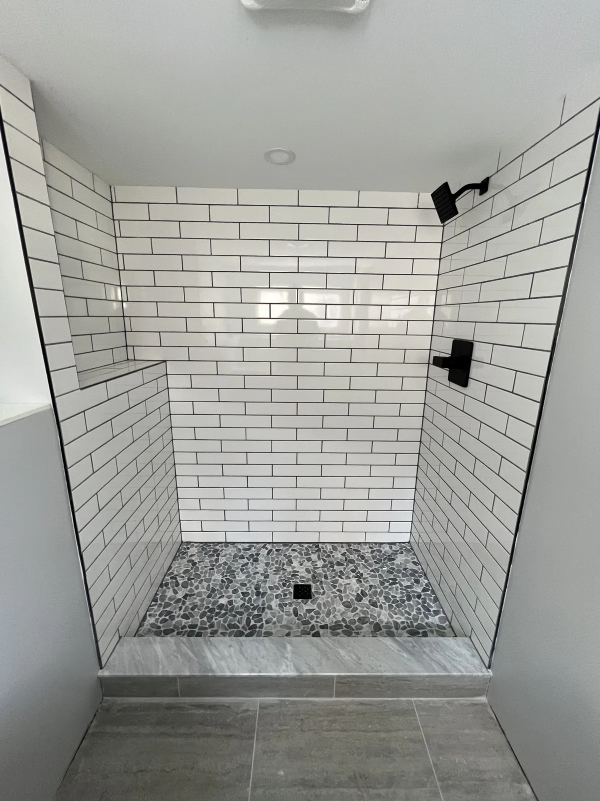 Shower lined in white subway tile with a mosaic floor and a tiled niche