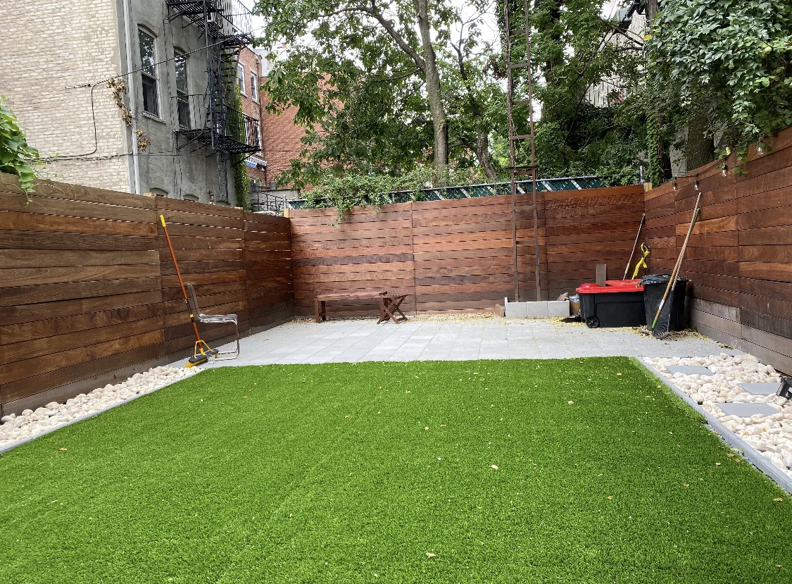 Small back yard laid with artificial turf inside a stained timber fence